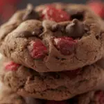 Plate of cherry chocolate chewy cookies stacked with chocolate chips and cherries