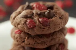 Plate of cherry chocolate chewy cookies stacked with chocolate chips and cherries