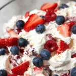 Red, white, and blue cheesecake salad in a glass bowl with berries and marshmallows.