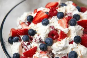 Red, white, and blue cheesecake salad in a glass bowl with berries and marshmallows.